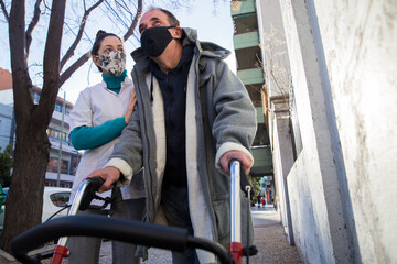 Fototapeta na wymiar Female nurse supporting elderly man with walker outside wearing protective mask after Covid19 recovering.