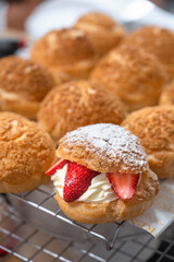 Homemade Craquelin Choux biscuits (crispy cream puffs) with cream filling and Strawberries on rack.