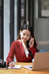 Attractive businesswoman sitting at her workplace and talking on mobile phone.
