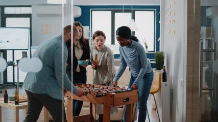 Frustrated man losing foosball game having fun after work at office. Woman beating person while playing football at play table, enjoying bottles of beer and leisure with colleagues