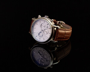 Unbranded hand watch with brown leather strap on black glassy surface, closeup. Product photography...