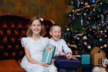 Girl and boy with gifts under the Christmas tree. Children laugh. Children are happy. A girl and a boy are happy with new year's gifts.