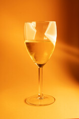 glass of white wine on orange background with lights on glass