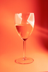 glass of pink wine on red background with lights on glass