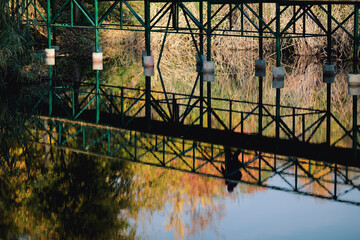 Reflection in water of people walking over a pedestrian bridge in a park during a sunny autumn day.