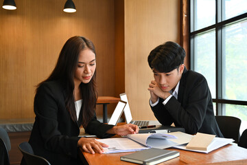 Photo of young business developer team working together at the wooden table surrounded by a paperwork and white blank screen computer laptop.