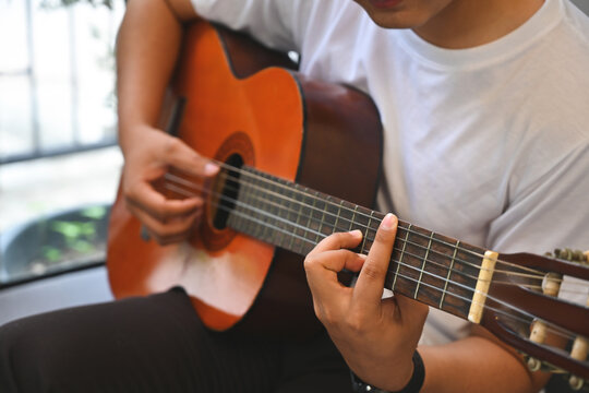 Cropped image of young guitar artist playing guitar while sitting and relaxing on the living room sofa.