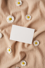 Blank clipping path paper sheet card with mockup copy space, chamomile flower buds on neutral beige muslin cloth. Minimal aesthetic business brand template. Flat lay, top view