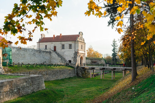 Ancient stone castle among tall trees. Castle with a stone bridge and a cozy courtyard with green grass. The fortress is surrounded by a yellow autumn park.