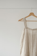 Minimalist wardrobe: Neutral beige colour overall dress or sundress on hanger against white wall. Aesthetic fashion concept