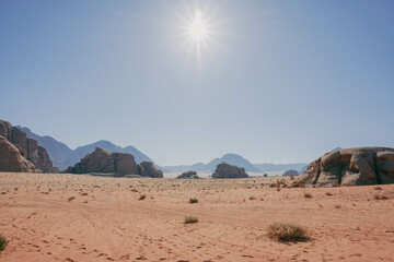 Fototapeta na wymiar Wadi Rum desert, mountains are on the horizon, car tracks are on the sand, clear cloudless sky, sun with rays, Jordan