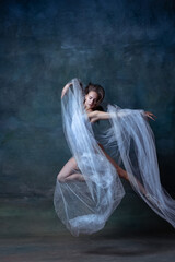 Studio shot of young flexible ballerina dancing isolated on dark vintage studio background. Art, motion, action concept.