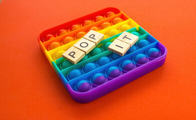 A colorful pop it game on a bright orange background. The inscription pop it with wooden booms. selective focus. Popular children's toy