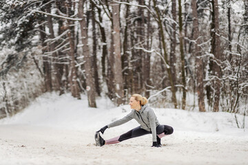 Flexible sportswoman doing stretching and warmup exercises in woods at snowy winter day. Healthy lifestyle, outdoor fitness