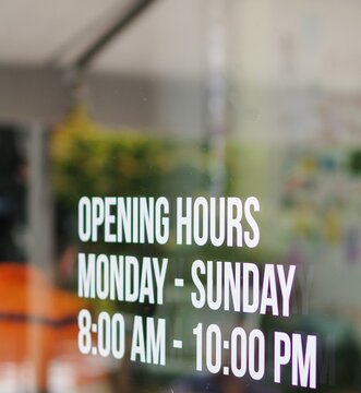 Opening hour sign white decal sticker on store window glass. Monday to Sunday. 8 am to 10 pm.