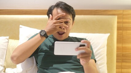 Shocked and surprised funny face of Asian man watch the smartphone alone at night.