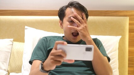 Shocked and surprised funny face of Asian man watch the smartphone alone at night.