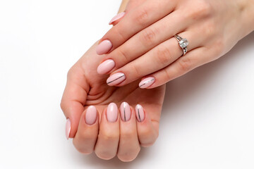 Nude, beige, natural manicure with a silver strip on long oval nails close-up on a white background. A beautiful ring, decoration.