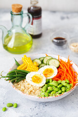 Obraz na płótnie Canvas Healthy salad with couscous, carrots, cucumber, green beans, soybeans, corn and an egg on a gray concrete background. Food and health. Buddha bowl salad. Organic natural food. Plant-based dishes.