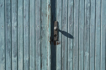 Altes Holz Tor mit Sicherheitsschloss und Türknauf. Die früher moderne Farbe ist sonnengebleicht und blättert an vielen Stellen ab.