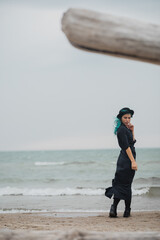 beautiful woman with blue hair and hat walks on the windy beach