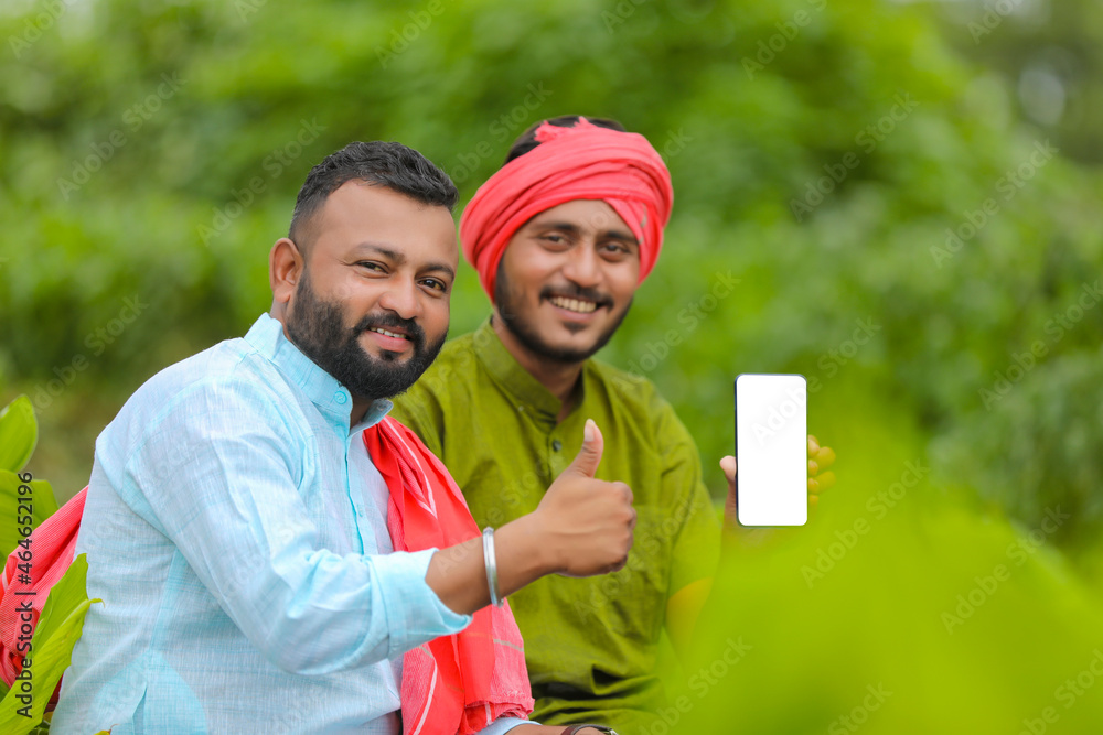 Poster Indian farmers showing smartphone at green turmeric agriculture field.