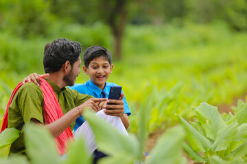 Fototapeta premium Indian farmer using smartphone with his child at green turmeric agriculture field.