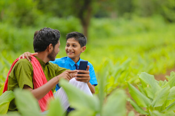 Naklejka premium Indian farmer using smartphone with his child at green turmeric agriculture field.