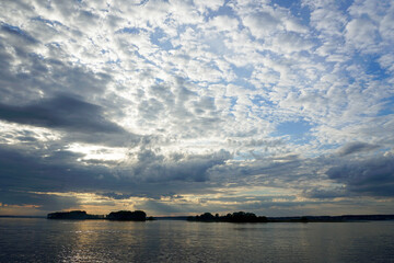 Sunset over the lake on a warm summer day. June sky and beautiful clouds. Horizon and reflection. The smooth surface of the water.	
