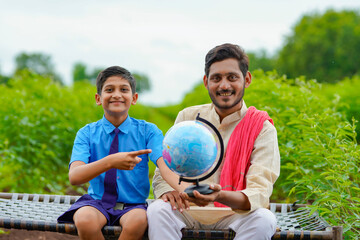 Indian farmer holding world globe in hand and giving some information to his child