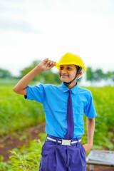 Cute Asian Indian little child wearing yellow construction helmet or safety hard hat.