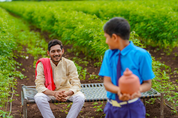 importance of saving concept : Smart indian little boy standing and holding piggy bank in hand with his father at agriculture field.