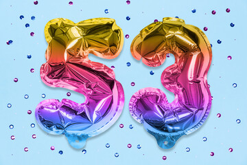 Rainbow foil balloon number, digit fifty three on a blue background with sequins. Birthday greeting card with inscription 53. Top view. Numerical digit. Celebration event, template.