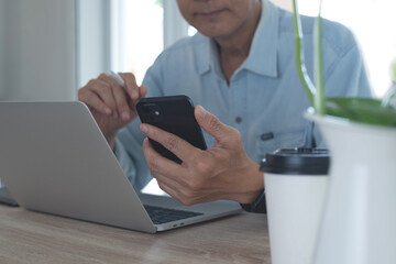 Asian business man using mobile phone, thinking about his work project during working on laptop computer with digital tablet on table at home office