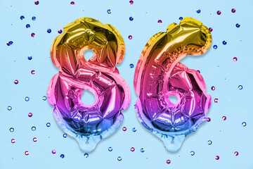 Rainbow foil balloon number, digit eighty six on a blue background with sequins. Birthday greeting card with inscription 86. Top view. Numerical digit. Celebration event, template.