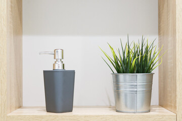 Soap dispenser and artificial houseplant on shelf in bathroom