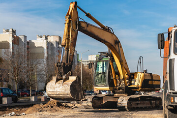 An excavator in a modern city is carrying out work during the reconstruction of the road. Repairs in the city with heavy construction equipment.