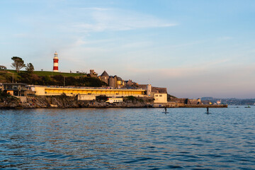 Paddle boarders on the water during sunset with lighthouse in the background, Plymouth Devon