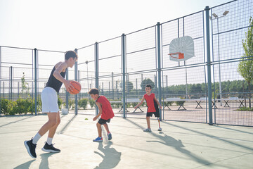 Basketball trainer play basketball with two children, one has a leg prosthesis.