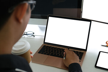 Behind view of a businessman holding a coffee cup while using a white blank screen computer laptop...