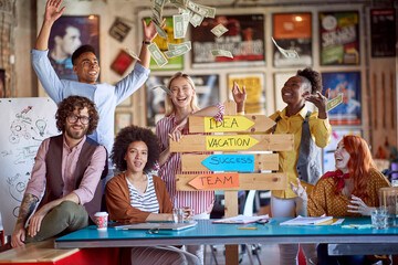 Group of young creative people is throwing money while posing for a photo at their workplace