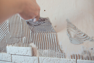 A worker applies tile adhesive to the wall, makes repairs in the apartment. The builder applies the plaster with a trowel. plaster on the wall. stick decorative tiles on the wall