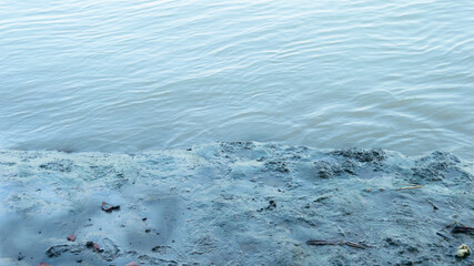 Muddy river banks in low tide next to wave water. Alluvial soils deposited by the river. Nature background. Close up.