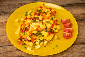 Fresh Omelette with cheese and greens and tomatoes on yellow plate on wooden table texture