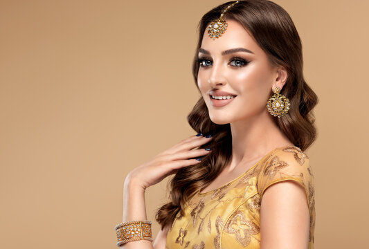 Portrait of beautiful indian girl. Young hindu woman model with golden kundan jewelry set, earrings, tikka and bracelet . Traditional India costume lehenga choli or saree . Curly hair