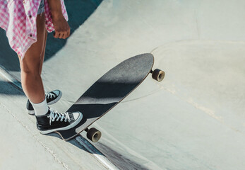 close-up detail of a girl holding her skateboard with one foot before launching herself down a slope. skateboarding and fun concept.selective focus on the skateboard.