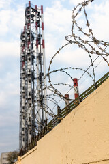 barbwire on yellow fence and factory pipes and blue sky with white clouds on background (focus on the wires)
