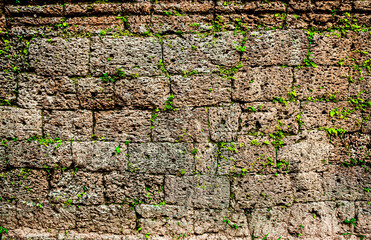Stone masonry of walls and fences of ancient fortress structures covered with green moss. The ancient city of Angkor wat in Cambodia. Background wall with texture of green moss and plants.