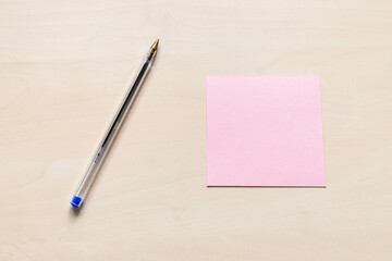 top view of blank pink sheet of note paper and blue pen on light brown wooden board