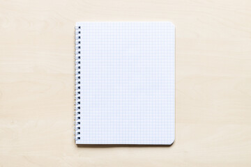 top view of blank sheet of squared paper of spiral notebook on light brown wooden board